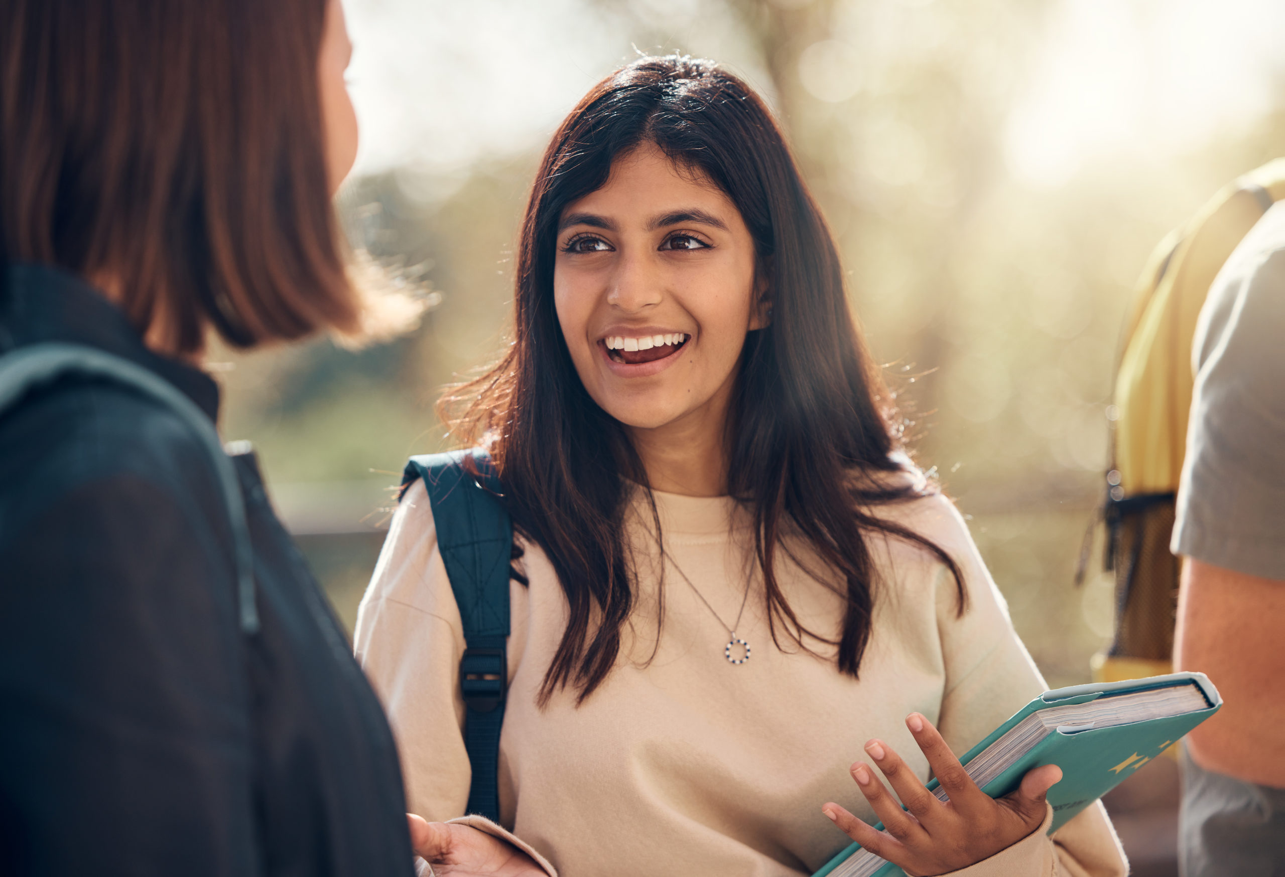 Happy, university and woman student from India laughing and talking about a test. College, book and happy woman speaking to campus students about education, learning and school studying with a smile.