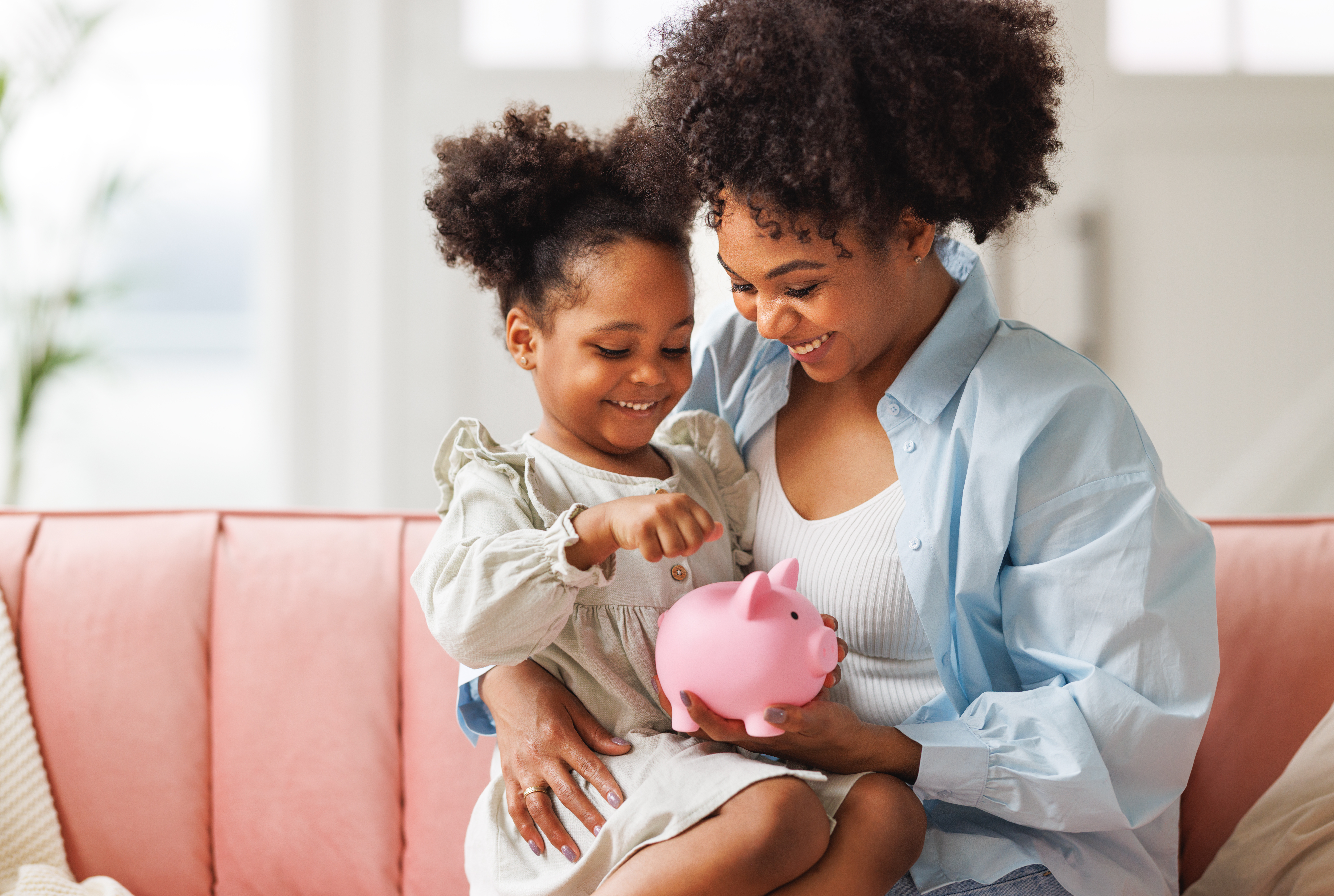 Mom teaching daughter how to save money in a piggy bank.